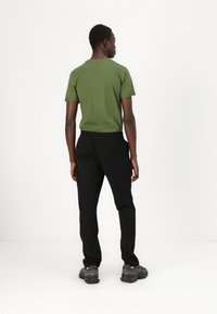 Green short-sleeve t-shirt paired with black elastic-waist pants, viewed from the back, worn with black athletic shoes on a plain background.