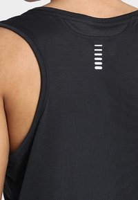 Top noir sans manches avec une texture lisse, présentant un design de dos unique avec des rayures blanches horizontales pour la ventilation.