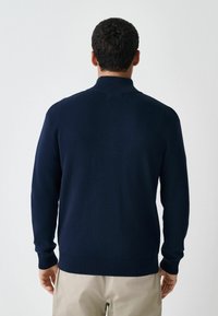 Navy knitted sweater with a high collar, ribbed cuffs, and hem. Made from soft material, featuring a seamless back design.