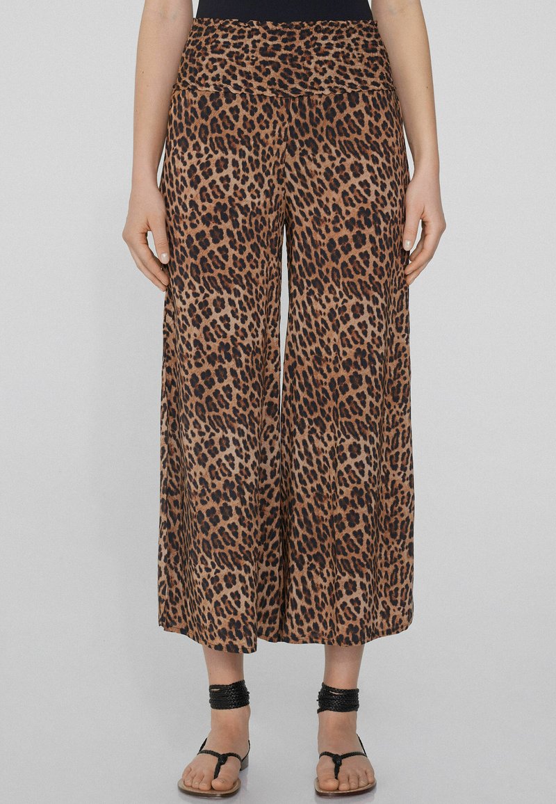 Bruine luipaardprint wijde broek van een zachte, lichtgewicht stof met een hoge tailleband. Gemaakt in combinatie met zwarte platte sandalen en enkelsieraden.