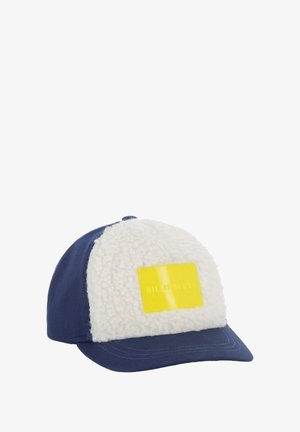 Marineblauwe pet met een witte pluizige voorpaneel, voorzien van een rechthoekige gele patch met de tekst "BILLIEBLUSH" reliëf. Zachte textuur, gebogen klep.