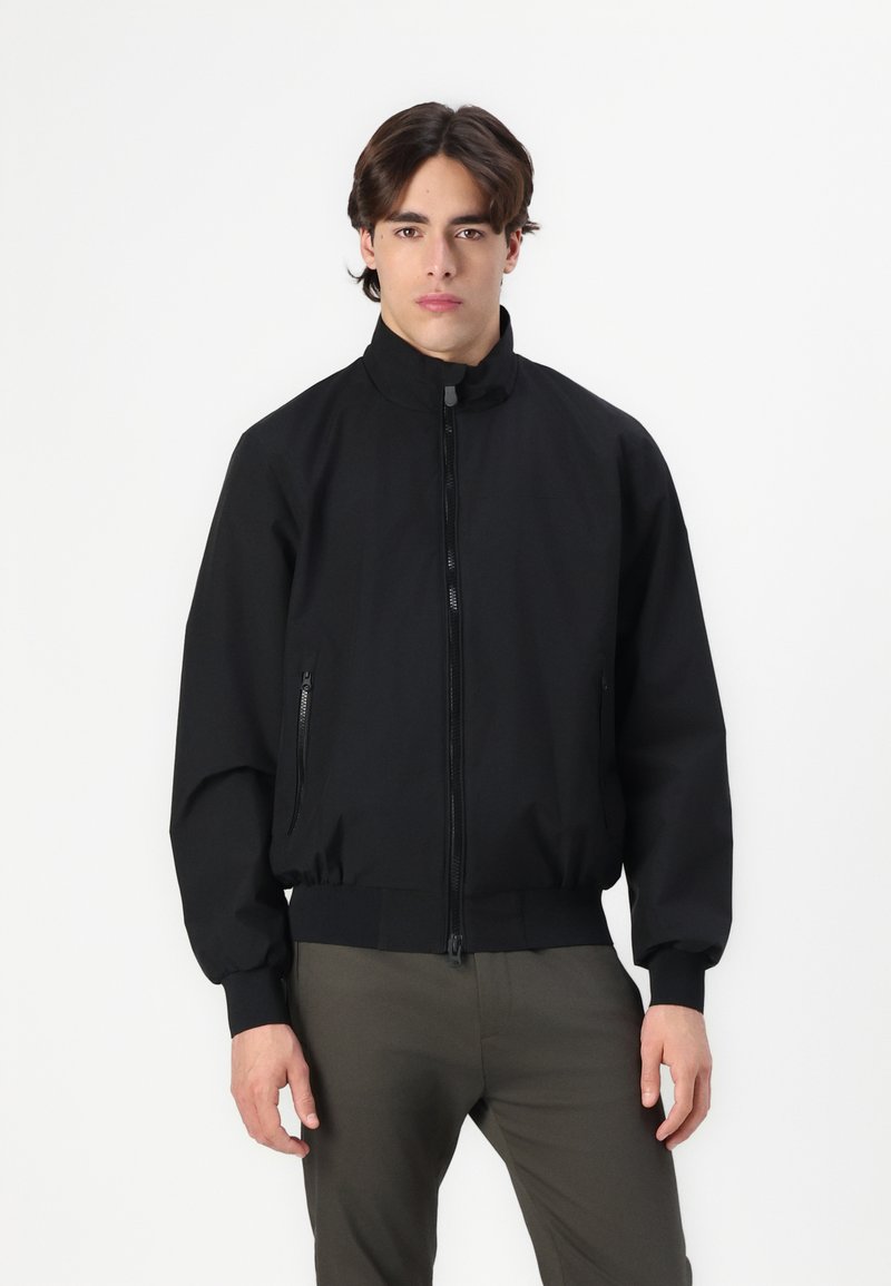 Black bomber jacket with a stand-up collar, zipper front, and side pockets. Features elastic cuffs and waistband, made of smooth fabric.