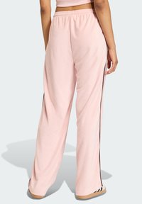 Pink, loose-fitting sweatpants with a textured fabric, elastic waistband, and black side stripe detailing. Flat, open hems.