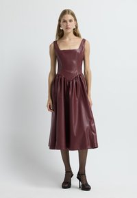 Vestido de cuero burdeos con escote cuadrado, corsé ajustado y falda con frunces. Presenta una textura suave y tirantes anchos.