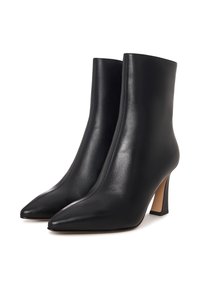 Botas de cuero negro hasta el tobillo con puntas afiladas y tacones de bloque de altura media, mostradas una al lado de la otra sobre un fondo blanco.