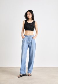 Svart avkortet tanktopp med elastisk kant og rødt logo, kombinert med høy livet lyseblå jeans. Modellen har på seg svarte høye hæler.