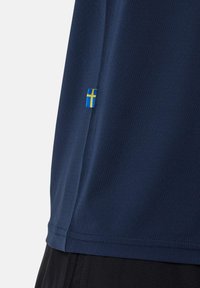 Marine sportsbluse med korte ærmer, lavet af åndbart stof, med et lille svensk flag label i kanten.