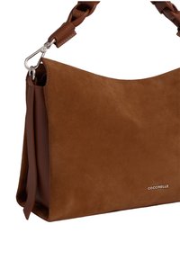 Bruine suède handtas met een zachte textuur, voorzien van een gevlochten leren schouderband en zilveren hardware. Logo elegant weergegeven op de voorkant.