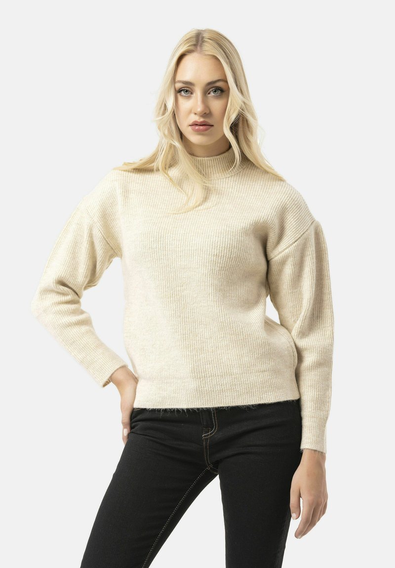 Crèmekleurige gebreide trui met een hoge hals, geribbelde structuur en verlaagde schouders. Gecombineerd met zwarte jeans met gele stiksels.