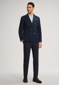 Marineblauwe double-breasted blazer van gestructureerde stof met zilveren knopen, gecombineerd met bijpassende broek en bruine enkellaarsjes.