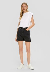 Shorts en denim noir avec ourlets retournés, associés à un t-shirt blanc ample et des baskets blanches, sur fond gris uni.