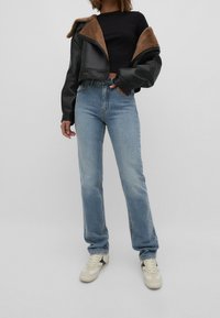 Černá kožená zkrácená bunda s hnědým ovčím rounem, v kombinaci s světle modrými rovnými džíny a smetanovými teniskami s černými akcenty.