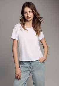 Wit T-shirt met korte mouwen en een ronde hals, gecombineerd met lichtblauwe high-waisted jeans, met een ontspannen pasvorm en minimale details.
