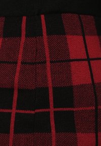 Tissu tricoté en tartan rouge et noir avec des lignes verticales et horizontales épaisses et fines se croisant, formant un motif à carreaux.