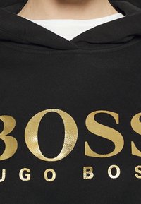 Sudadera con capucha negra con grandes letras metálicas doradas que dicen "BOSS HUGO BOSS". Tejido suave con capucha ajustable con cordón.
