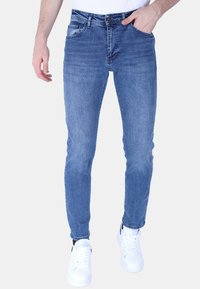 Blauwe denim jeans met een slim fit, voorzien van voorzakken en een vervaagde wassing. Gecombineerd met witte sneakers, geshowd tegen een effen achtergrond.