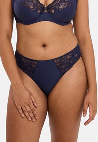 Ensemble de lingerie bleu marine composé d'un soutien-gorge en dentelle avec armatures et d'un string assorti à bordures en dentelle, présentant des motifs floraux délicats.