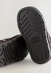 Suole di scarpe in gomma nera con un motivo di battistrada testurizzato, con un logo in rilievo che recita "NEXT UK 6" vicino al centro.