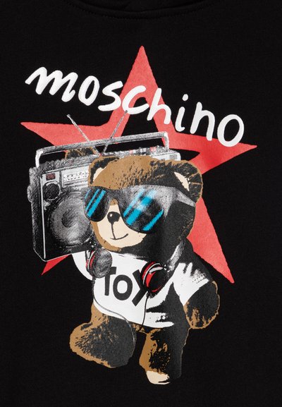 Un tejido negro presenta un oso de dibujos animados que lleva gafas de sol y auriculares, sosteniendo un boombox, con una estrella roja y el texto "Moschino" arriba.
