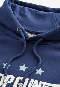 Felpa blu navy con cappuccio e cordino, dotata di occhielli in metallo. Il testo riporta "TOPGUN" in bianco, con stelle azzurro chiaro affiancate al testo.