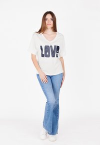 Camiseta blanca de cuello en V con estampado en navy de "LOVE", combinada con jeans acampanados de color azul claro y zapatillas blancas; tejido suave, corte relajado.