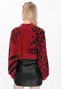 Rdeča puhasta krajšana jopica z črnim leopardjim motivom in stripe obliko. V kombinaciji z črno usnjeno mini krilom, ki prikazuje teksturiran zaključek.