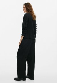 Maglione nero a maglia con polsini a coste abbinato a pantaloni neri a gamba larga con ricami floreali di lato e stivaletti di pelle alla caviglia.