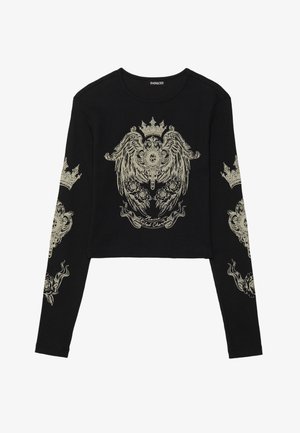 Crop top noir à manches longues avec une texture côtelée. Présente des motifs graphiques dorés complexes de couronnes et de roses sur le devant et les manches.
