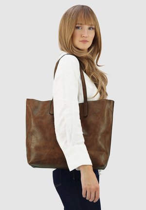 Bruine leren tote bag met een gestructureerd oppervlak, open bovenkant en twee lange schouderbanden, weergegeven tegen een neutrale achtergrond.