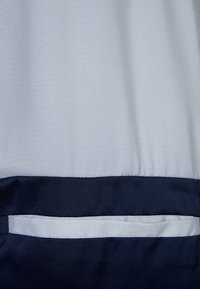 Ljusgrått tyg med en slät textur som har en marinblå accent längst ner. Inkluderar en horisontell fickdetalj.