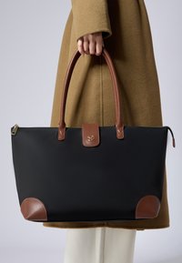 Černá taška přes rameno s hnědými koženými detaily, zaoblenými rohy, klopovým uzávěrem a dvojitými uchy. Hladká textura, elegantní design.