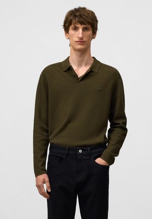 Olijfgroene polo-shirt met lange mouwen, voorzien van een textuurpatroon en een kraag, gecombineerd met donkerzwarte pantalon. Knoppen zichtbaar op de kraag.