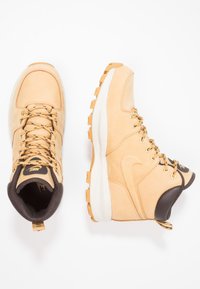 Bottes de randonnée Nike en cuir beige clair avec des accents marron. Possèdent des œillets dorés, des lacets noirs et des semelles en caoutchouc texturé pour une meilleure adhérence.