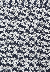 Marineblaues Gewebe mit einem weißen floralen Muster, das verschiedene Blumenformen und -größen zeigt. Leichte, weiche Textur mit einem leichten Glanz.