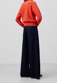 Oranje gebreide trui met geribde manchetten, gecombineerd met wijde donkere denim jeans met een rafelige zoom en twee achterzakken.
