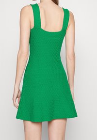 Abito verde lavorato a maglia con un motivo testurizzato, schiena quadrata, spalline larghe e gonna svasata. Progettato per una silhouette aderente.