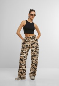 Crni crop top i bež vojnog uzorka trenirke s vezicom, koje imaju širok kroj i bočne džepove, uparen s sivim tenisicama.