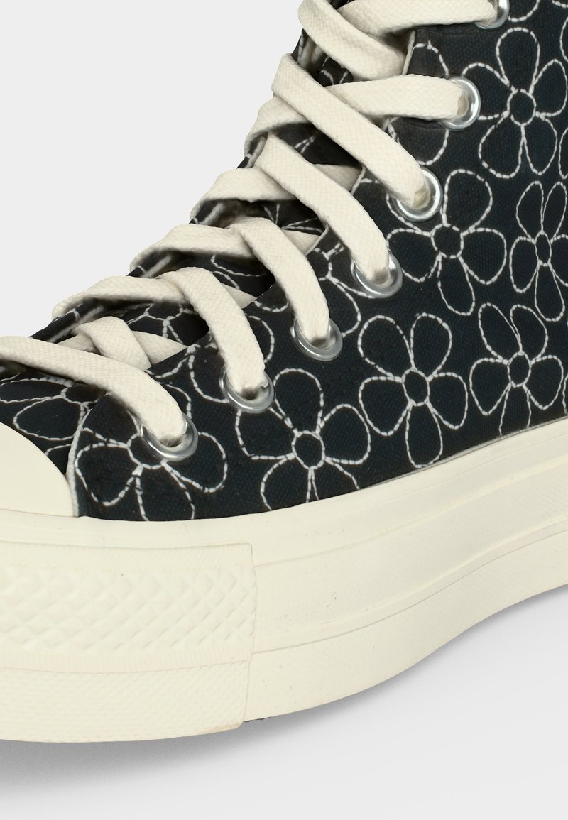 Schwarzer High-Top-Sneaker mit weißem Blumenmuster, weißen Schnürsenkeln und elfenbeinfarbener Gummisohle und Zehenkappe.