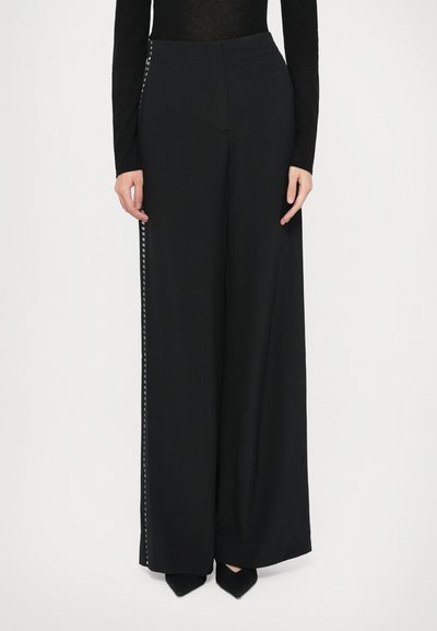 Pantaloni neri a gamba larga realizzati in tessuto liscio, con dettaglio laterale a motivo geometrico bianco. Vita alta e taglio a tutta lunghezza.
