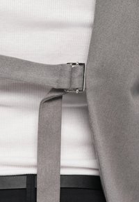 Gray fabric belt with a silver metal buckle, secured around a white ribbed shirt. Features clean lines and a smooth texture.