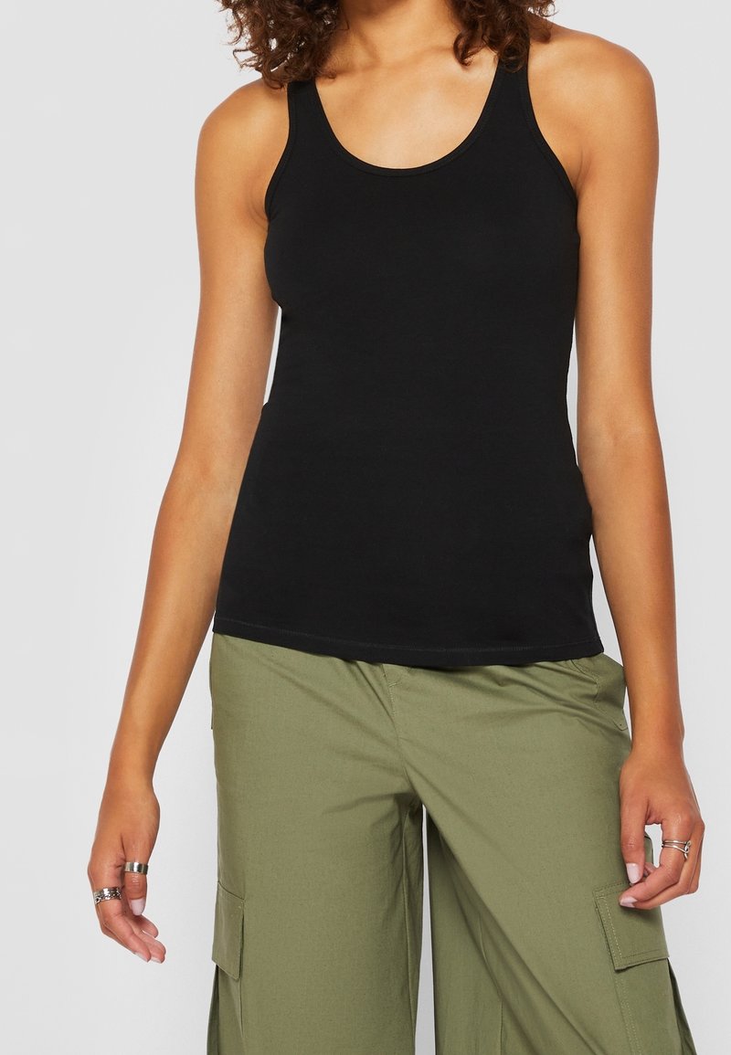 Débardeur noir avec un col arrondi et des bretelles fines. Associé à un pantalon cargo vert avec des poches latérales et une coupe décontractée.