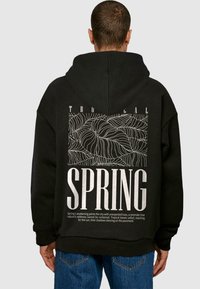 Sort hættetrøje med et stort hvidt grafik; har et plante-design og ordet "SPRING" i fed skrift. Stof ser blødt ud med en afslappet pasform.