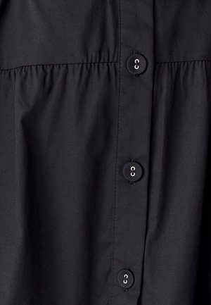 Mustade nuppude ja viie nööbiga shirt, millel on kokku pandud tekstuur rinnaaluselt, sileda kangast viimistlusega.