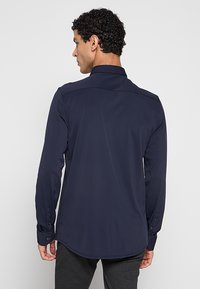 Marineblauw shirt met lange mouwen gemaakt van gladde stof met een klassieke kraag, zichtbare naden en knoopmanchetten, uitgerust met een gebogen zoom.