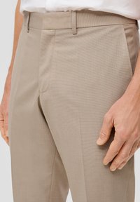 Pantalones de vestir beige con una textura suave, que presentan un frente plano, bolsillos laterales y un diseño de corte slim.