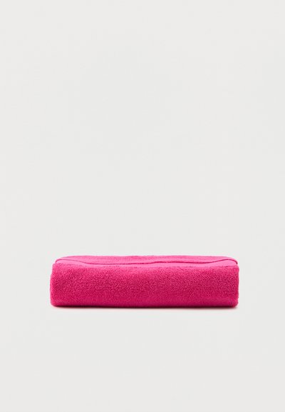 Folded bright pink terry cloth towel resting on a plain light gray surface.