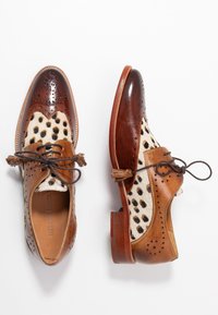 Oxfords en cuir marron avec un panneau en cuir de veau à pois, fermeture à lacets et perforations décoratives. Le talon en bois crée un contraste.