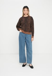 Sweater com padrão de leopardo castanho, com um decote e punhos canelados, combinado com calças de ganga azuis de cintura alta e largas, e sapatos baixos pretos.