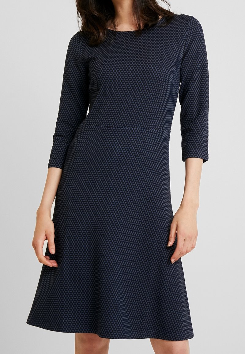 Robe bleu marine à manches trois-quarts, jupe évasée, motif texturé de petits losanges, encolure ronde et tissu lisse.