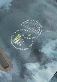 Tissu à motifs bleus et gris avec un graphique circulaire comprenant du texte et un design de globe. Comprend une section zippée le long d'un bord.